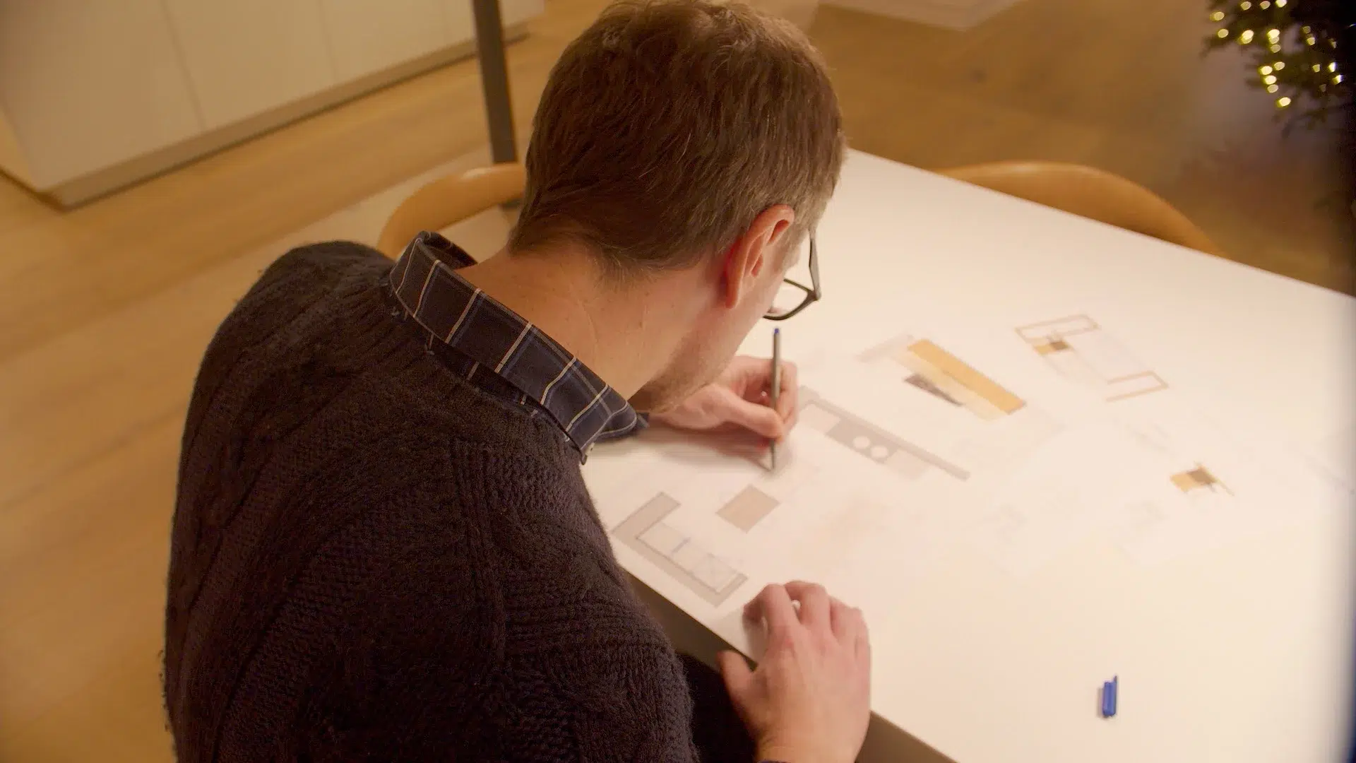 Kitchen designer sketching a kitchen layout and reviewing material samples on a large plan.