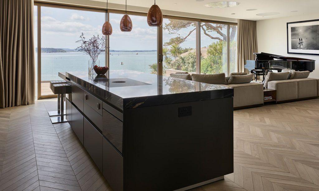 Kitchen island aligned with full-height glazing and an outdoor terrace, showing the route between inside and outside.