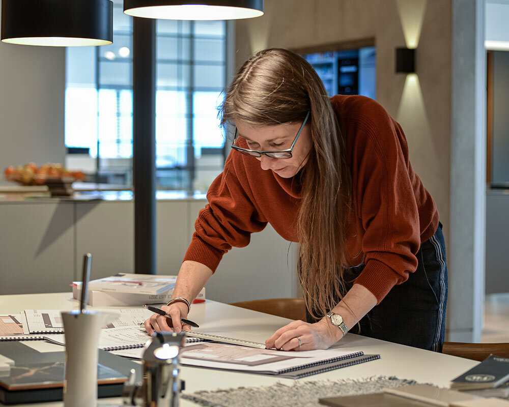 Hands reviewing a kitchen floor plan and material samples during a design meeting.