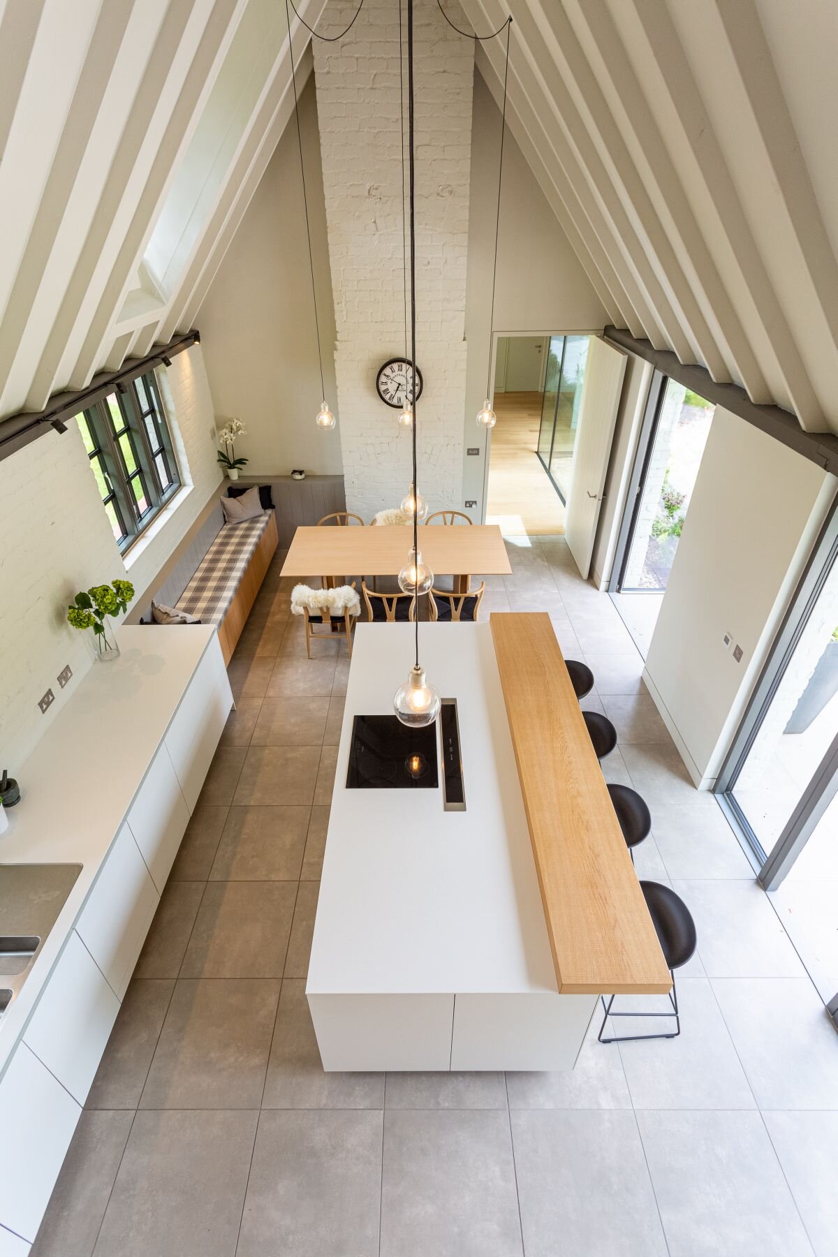 High-level view along a long kitchen with a white island, timber breakfast bar and dining area beneath a pitched roof.