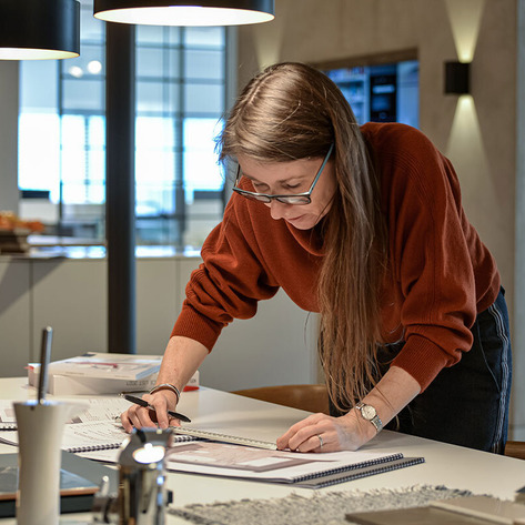 Hands reviewing a kitchen floor plan and material samples during a design meeting.