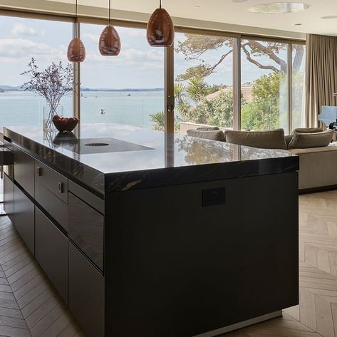 Kitchen island aligned with full-height glazing and an outdoor terrace, showing the route between inside and outside.