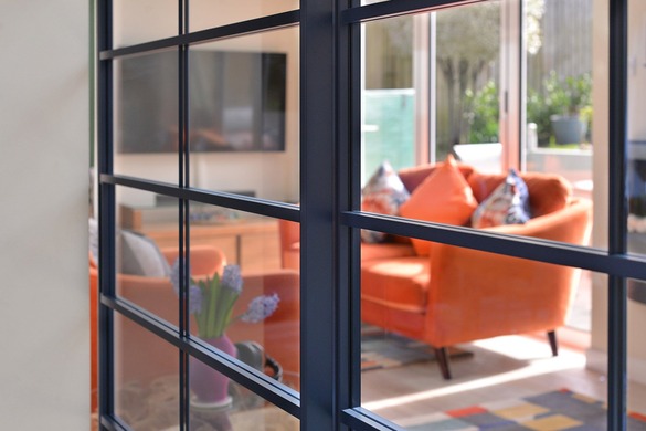 Close-up of a Rimadesio Soho glass panel and dark aluminium grid with a warm-toned living area visible beyond