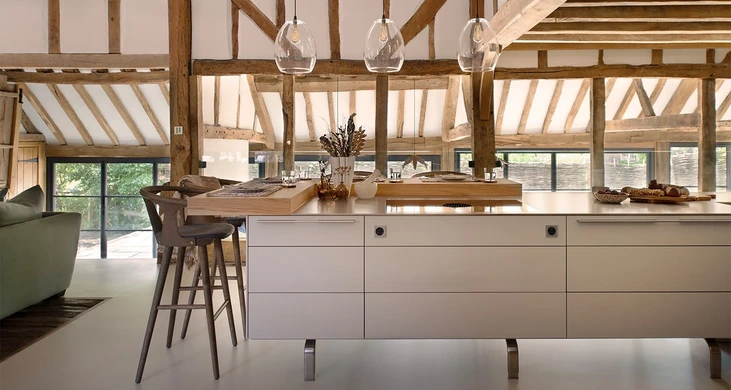 Light-filled kitchen in a converted timber barn, with a pale-grey island, exposed beams and pendant lighting.