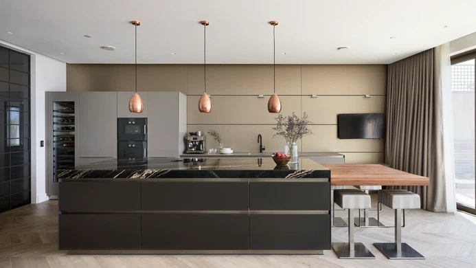 Modern dark kitchen with large island and copper pendant lights and quartz worktop.