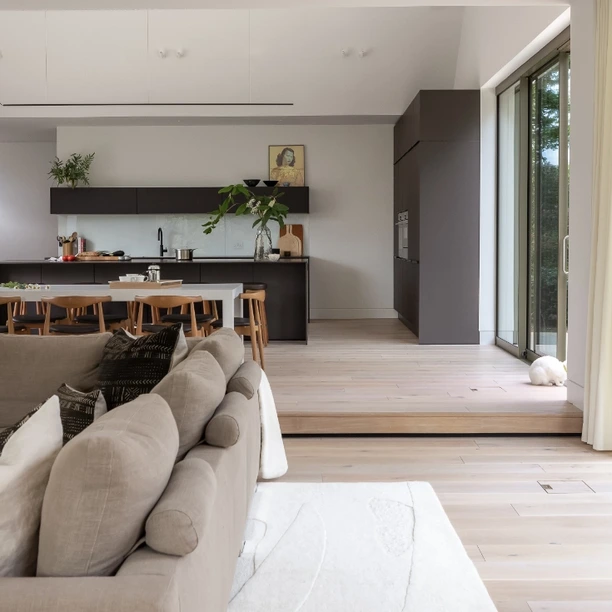 Handleless dark brown kitchen cabinetry with integrated ovens in open plan space
