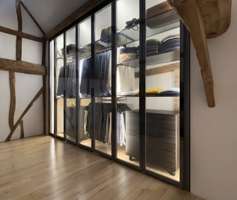 Floor-to-ceiling glass wardrobe with illuminated hanging rails and shelving