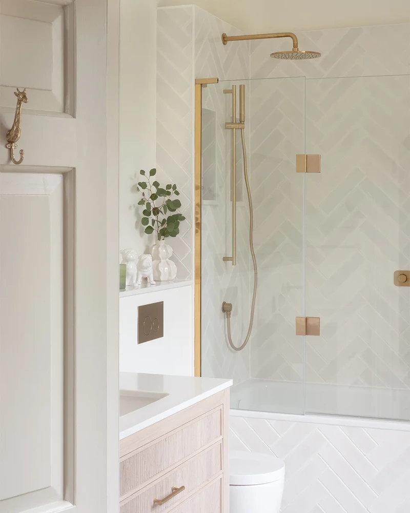 Full view of the ensuite showing the fluted vanity, toilet and glass shower enclosure with brass fittings.
