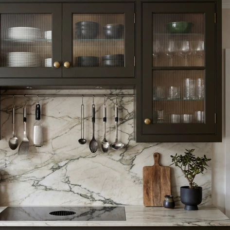 Dark glazed wall cabinets above a strongly veined stone splashback and preparation area.