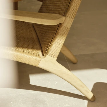 Close-up of a Carl Hansen & Søn pale oak chair frame and woven paper-cord seat, showing the curved rail and joinery.