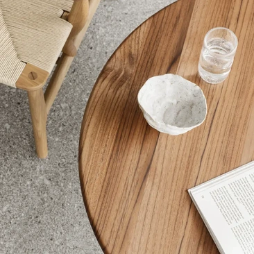 Rounded Carl Hansen & Søn timber coffee table with glassware and an open book, viewed from above beside a lounge chair.