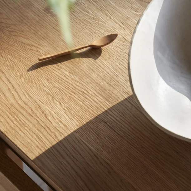Close-up of a Carl Hansen & Søn oak tabletop with a white ceramic bowl, showing the grain, rounded edge and strong shadow.