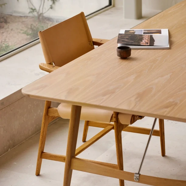 Timber Carl Hansen & Søn table beside an upholstered dining chair, with glassware and an open book on the surface.