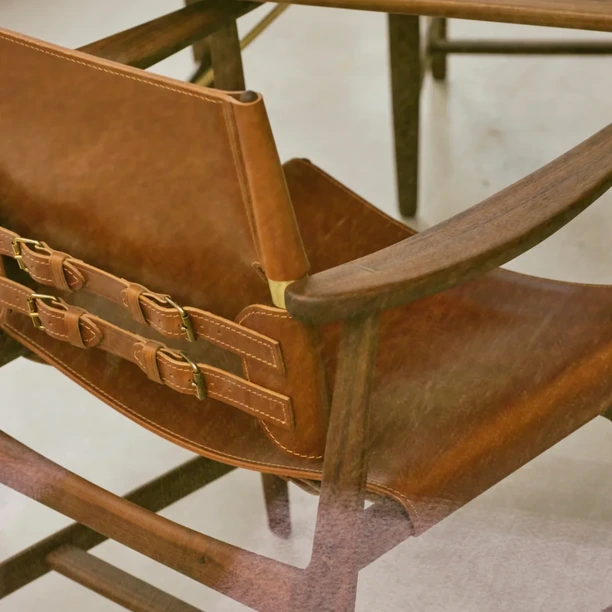 Close-up of a Carl Hansen & Søn timber-framed chair upholstered in dark leather, showing the seat, arm and joinery.
