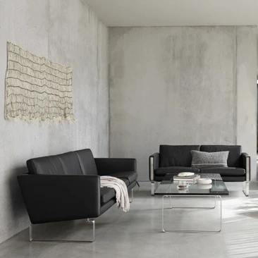 Black leather Carl Hansen & Søn sofa and lounge chairs arranged around low tables in a minimalist grey living room.