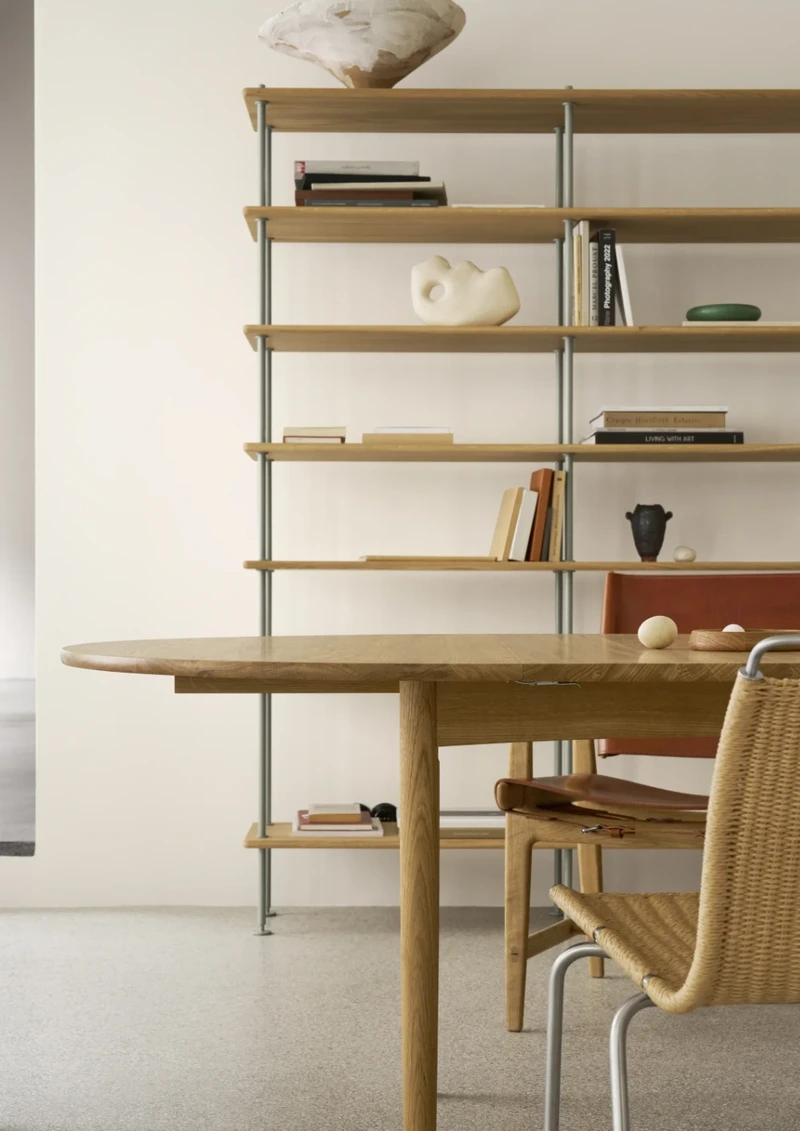 Carl Hansen & Søn wooden dining table and chairs positioned in front of full-height open shelving in a contemporary interior.