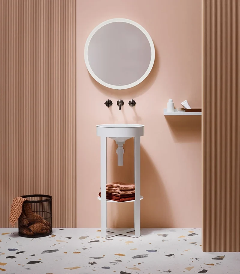 A slender bathroom vanity and sink area featuring a large round illuminated wall mirror