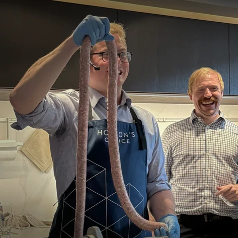 A Bath estate agent lifts a sausage whilst a Larkhill Butcher laughs in the background.