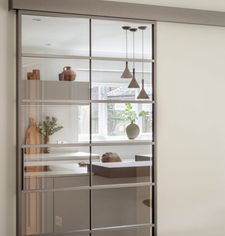Rimadesio Soho sliding glass door dividing an interior space, with shelving and pendant lights visible through the aluminium grid